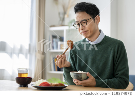 A man in his 40s staring thoughtfully at his fried chicken while eating A man in his 40s staring thoughtfully at his fried chicken while eating 119874978