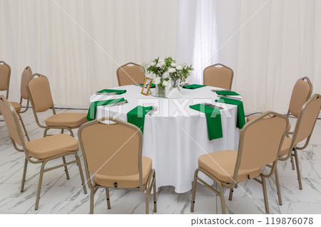 Wine glasses, silver tableware and green napkins on round tables covered with white tablecloth. Wine glasses, silver tableware and green napkins on round tables covered with white tablecloth. 119876078