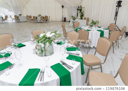 Wine glasses, silver tableware and green napkins on round tables covered with white tablecloth. Wine glasses, silver tableware and green napkins on round tables covered with white tablecloth. 119876106