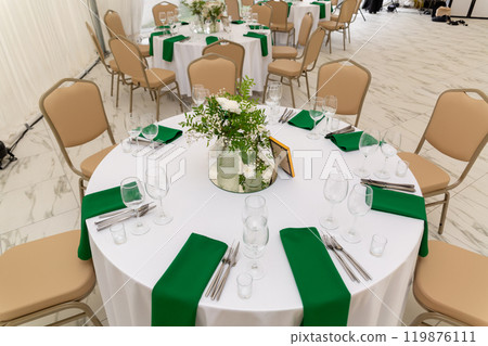 Wine glasses, silver tableware and green napkins on round tables covered with white tablecloth. Wine glasses, silver tableware and green napkins on round tables covered with white tablecloth. 119876111
