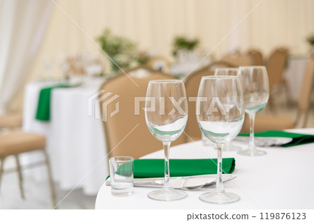 Close up of wine glasses, silver tableware and green napkins on round tables covered with white tablecloth. Close up of wine glasses, silver tableware and green napkins on round tables covered with white tablecloth. 119876123