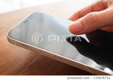 A woman's hand operating a smartphone on a desk A woman's hand operating a smartphone on a desk 119876752