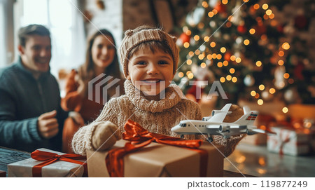 Happy joyful child boy with present, gift box in hands with a family at cozy home, decorated Christmas tree with garland lights. New Year celebration. This is AI-generated item 119877249