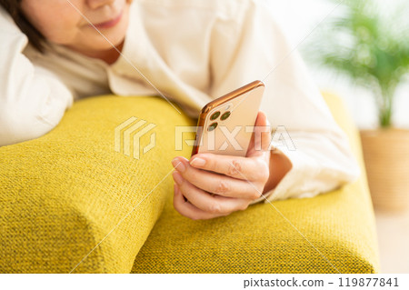 Middle-aged to senior woman lying on sofa looking at smartphone 119877841