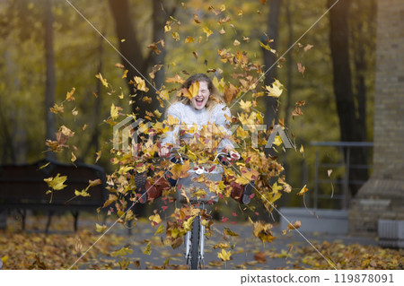 Young beautiful woman rides a bicycle in an autumn park under falling leaves. 119878091