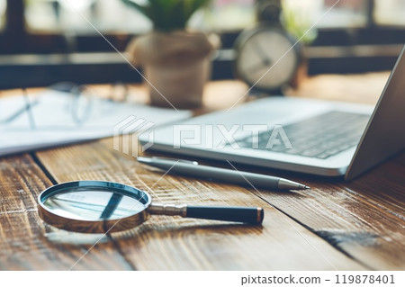 Laptop and magnifying glass on wooden table in office with copy space 119878401