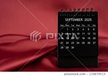 Black desk calendar for September 2025 on a red satin or silk textile background. 119879513