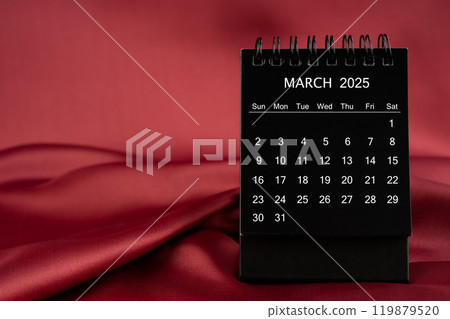 Black desk calendar for March 2025 on a red satin or silk textile background. 119879520