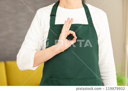 一位身穿綠色圍裙的高級女家庭主婦/管家在她家的客廳裡做一個圓圈標誌 119879932