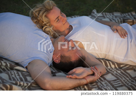 A beautiful middle-aged couple in love lies on the grass. A man and a woman are resting in nature. A beautiful middle-aged couple in love lies on the grass. A man and a woman are resting in nature. 119880375