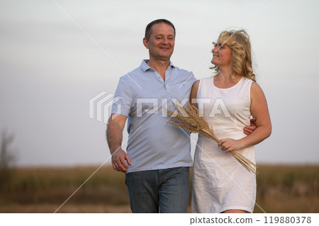 A beautiful middle-aged couple in love is walking in the field. 119880378