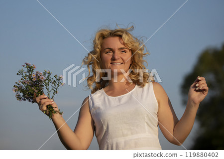 Beautiful middle-aged blonde with a bouquet of wildflowers against the blue sky. 119880402