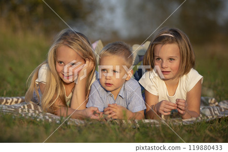 Sisters and little brother lie on the grass. Children play in the meadow. A happy family. 119880433
