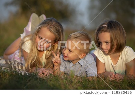 Sisters and little brother lie on the grass. Children play in the meadow. A happy family. 119880436