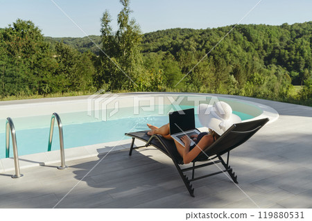 Woman working on laptop by poolside outdoors 119880531