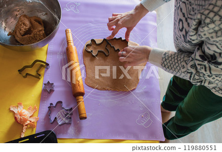 Woman in Christmas sweater making cookies with Christmas shape forms. Rolling pin, gingerbread dough and tangerine on the table. Christmas eve, top view. Pastry preparation. Homemade dessert. 119880551