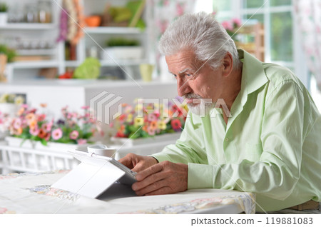 Elderly man posing at a table with a tablet Elderly man posing at a table with a tablet 119881083