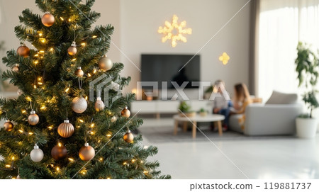 A beautiful Christmas tree in a house with a family playing in the background. 119881737