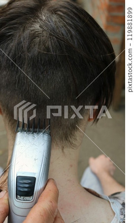 vertical photo of young man cutting hair with electric trimmer, close-up, hand with hair clipper cutting hair on back of teenager's head vertical photo of young man cutting hair with electric trimmer, close-up, hand with hair clipper cutting hair on back of teenager's head 119881899