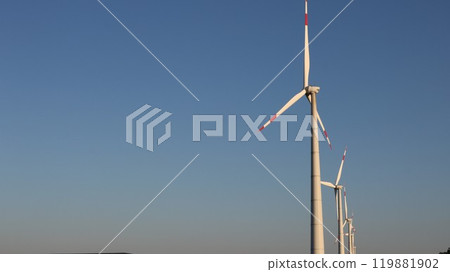 row of wind generators standing on the right side of the banner with blue background of light sky, windmills with large blades on the background of high clear sky with copy space row of wind generators standing on the right side of the banner with blue background of light sky, windmills with large blades on the background of high clear sky with copy space 119881902