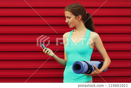 Fitness young woman with smartphone and yoga mat on red background 119881921