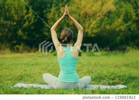 Young woman doing yoga exercises on a mat on the grass in summer park 119881922