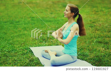 Young woman doing yoga exercises on a mat on the grass in summer park 119881927