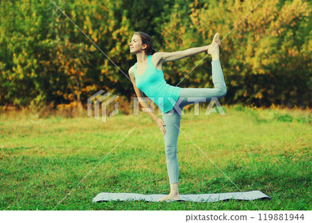 Fitness woman doing yoga exercises on a mat on the grass in summer park 119881944
