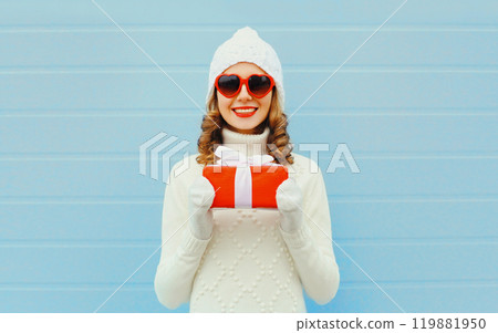 Christmas portrait happy smiling woman with gift box wearing a hat sweater over blue background 119881950