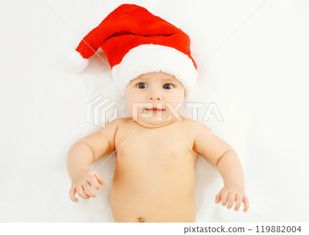 Christmas, family concept - cute baby in red santa hat lying on white bed home Christmas, family concept - cute baby in red santa hat lying on white bed home 119882004