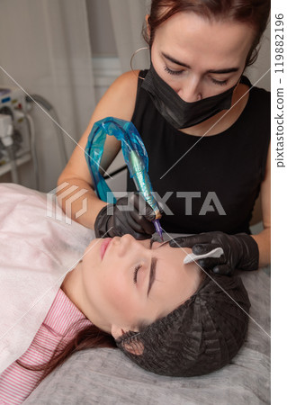 Beautician applying permanent makeup on eyebrows of client in beauty salon Beautician applying permanent makeup on eyebrows of client in beauty salon 119882196