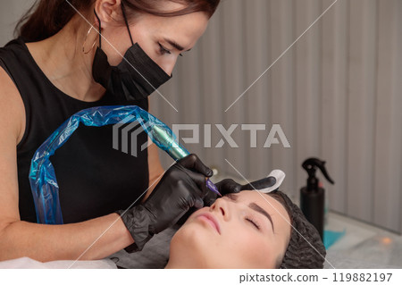 Beautician applying permanent makeup on eyebrows of client in beauty salon 119882197