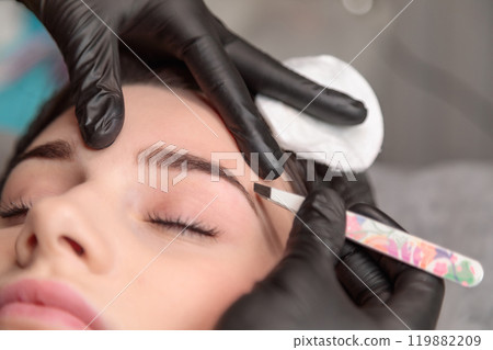 Beautician plucking eyebrows of client with tweezers in beauty salon 119882209