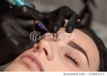 Cosmetologist applying permanent eyebrow makeup using tattoo machine 119882227