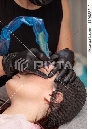 Beautician applying permanent makeup on eyebrows with tattoo machine Beautician applying permanent makeup on eyebrows with tattoo machine 119882241