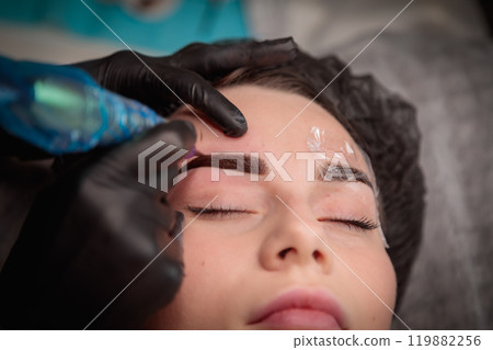 Cosmetologist applying permanent makeup on eyebrows  using tattoo machine 119882256
