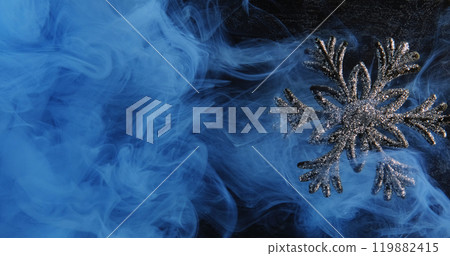 Abstract winter ornament. Snowflake mist. Blue color paint water smoke cloud revealing shiny glitter silver adornment on dark background. 119882415