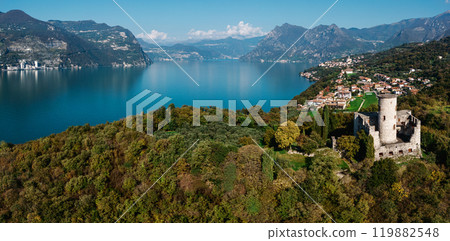 Aerial view of a historic stone tower on a lush hillside overlooking a serene blue lake 119882548