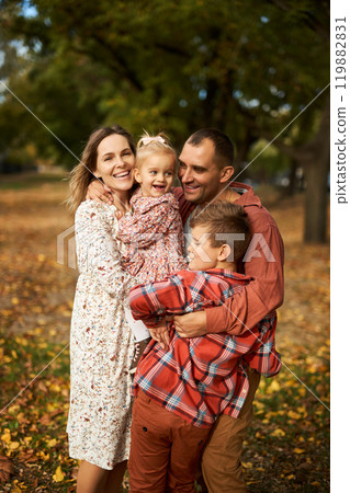 Happy family walking on green grass strewn with fallen leaves in Park in autumn. Parents, two Happy family walking on green grass strewn with fallen leaves in Park in autumn. Parents, two 119882831