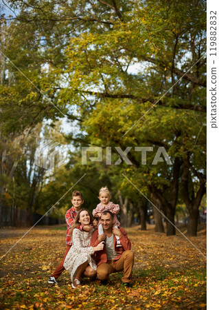 Happy family walking on green grass strewn with fallen leaves in Park in autumn. Parents, two Happy family walking on green grass strewn with fallen leaves in Park in autumn. Parents, two 119882832