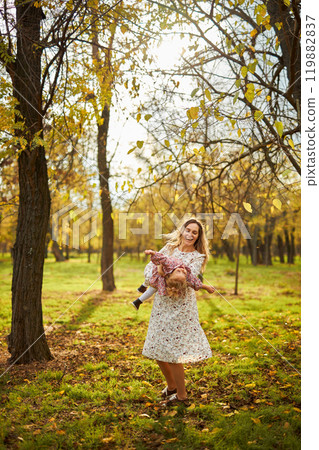 Beautiful happy mother playing with her child in sunny autumn park Beautiful happy mother playing with her child in sunny autumn park 119882837