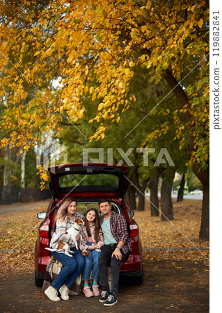 Happy parents with daughter and cute dog Jack Russel terrier sitting in car trunk on autumn day Happy parents with daughter and cute dog Jack Russel terrier sitting in car trunk on autumn day 119882841