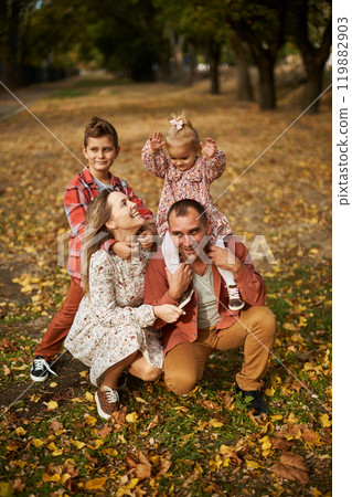 Happy family walking on green grass strewn with fallen leaves in Park in autumn. Parents, two 119882903