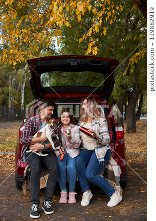 Happy parents with daughter and cute dog Jack Russel terrier sitting in car trunk on autumn day Happy parents with daughter and cute dog Jack Russel terrier sitting in car trunk on autumn day 119882919