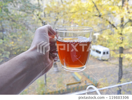 A cup of tea in your hand against the background of yellow autumn leaves 119883306
