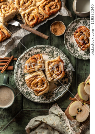 Autumn apple cinnamon rolls with frosting on green wooden background. Seasonal autumn homemade pastry cinnabons for breakfast Autumn apple cinnamon rolls with frosting on green wooden background. Seasonal autumn homemade pastry cinnabons for breakfast 119883340