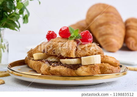 Croissant with banana pieces, chocolate paste in a round white plate Croissant with banana pieces, chocolate paste in a round white plate 119883512