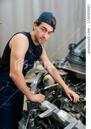 Vertical portrait of automotive mechanic male examining engine of old car. Serious vehicle service manager worker work in mechanics garage, check and maintenance to repair motorcar car in workshop. Vertical portrait of automotive mechanic male examining engine of old car. Serious vehicle service manager worker work in mechanics garage, check and maintenance to repair motorcar car in workshop. 119883661