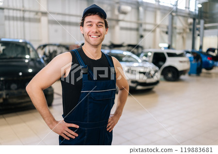 Medium shot portrait of cheerful technician male in uniform and cap standing posing auto service center, smiling looking at camera, enjoying time at workplace. Concept of professional car maintenance. 119883681