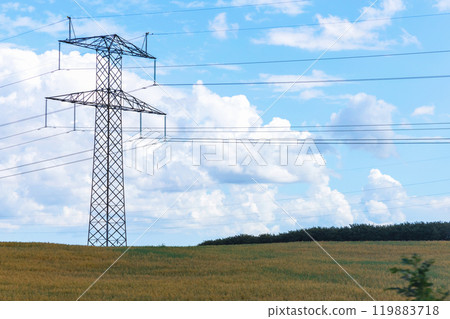 Electricity concept. High voltage power line pylons, electrical tower on a green field with blue sky. 119883718